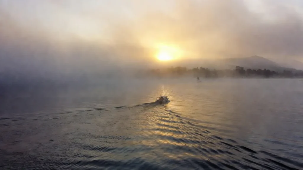 Person in small boat on misty lake at dawn representing recovery from emotional flashbacks in CPTSD and finding calm
